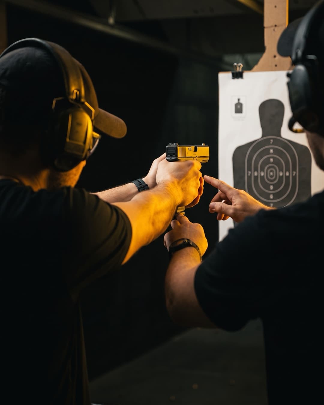 Schütze zielt mit einer Glock auf eine Papierscheibe, während der Instruktor seine Haltung korrigiert